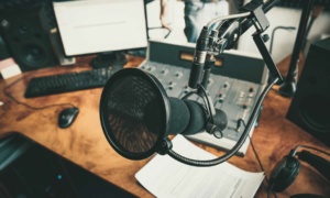 A professional voiceover studio showcasing a microphone in a recording setup, complete with a mixing console, computer screen, keyboard, and headphones on a polished wooden desk.