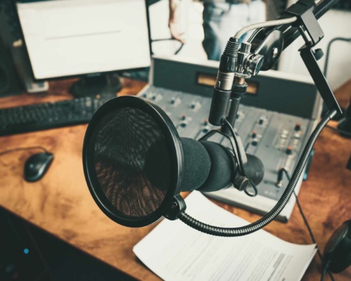 A professional voiceover studio showcasing a microphone in a recording setup, complete with a mixing console, computer screen, keyboard, and headphones on a polished wooden desk.