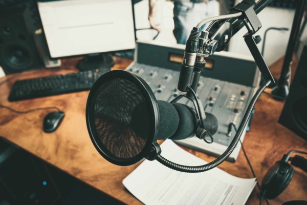 A professional voiceover studio showcasing a microphone in a recording setup, complete with a mixing console, computer screen, keyboard, and headphones on a polished wooden desk.